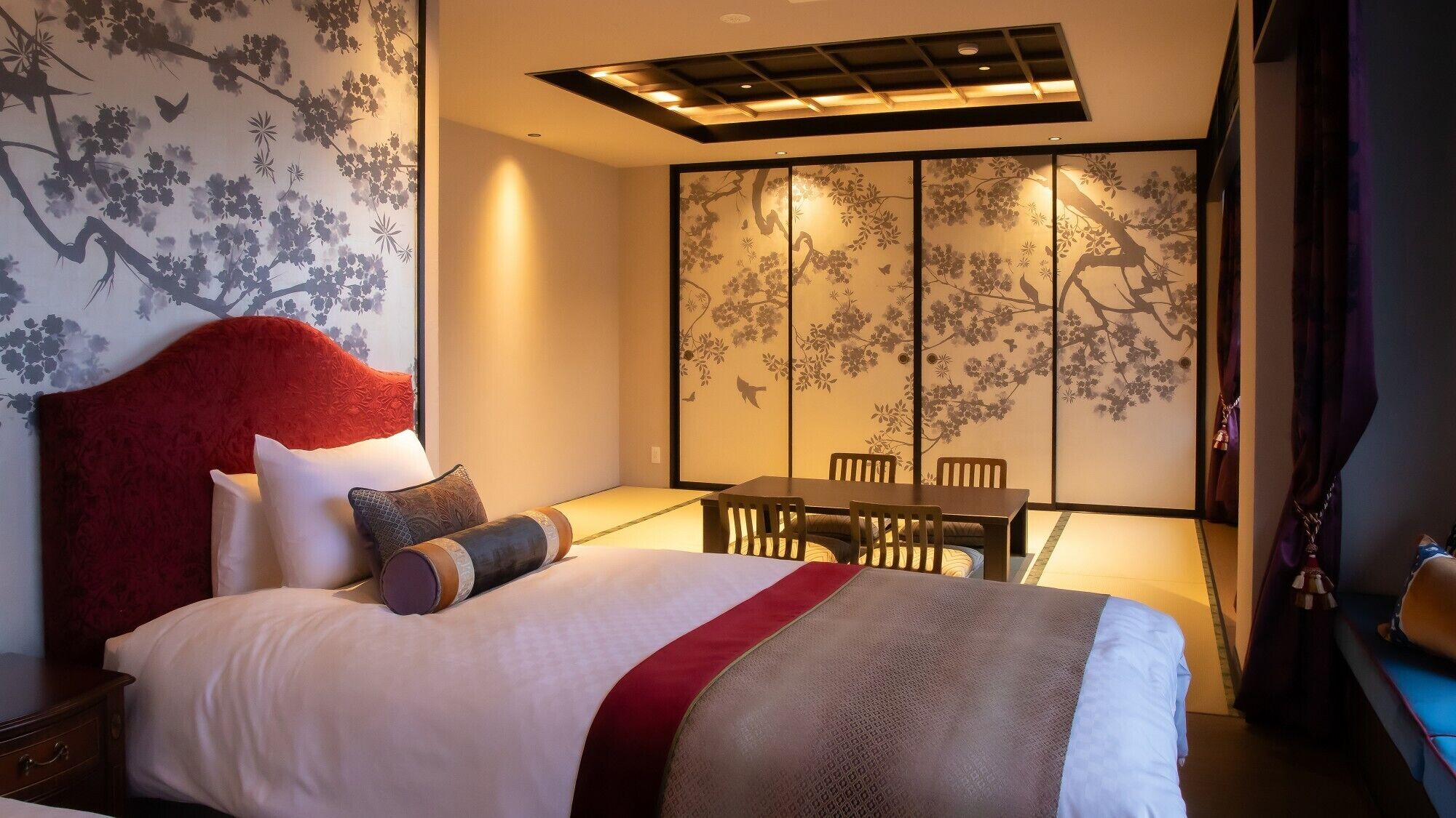 Une chambre d’hôtel comprenant un lit, une table à manger, des chaises et un paravent coulissant de style japonais orné de motifs floraux.