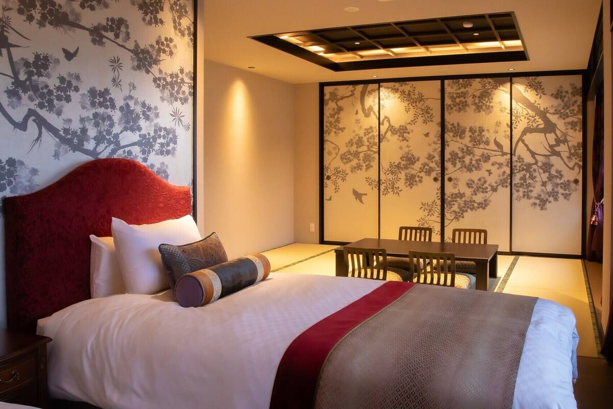 Une chambre d’hôtel comprenant un lit, une table à manger, des chaises et un paravent coulissant de style japonais orné de motifs floraux.