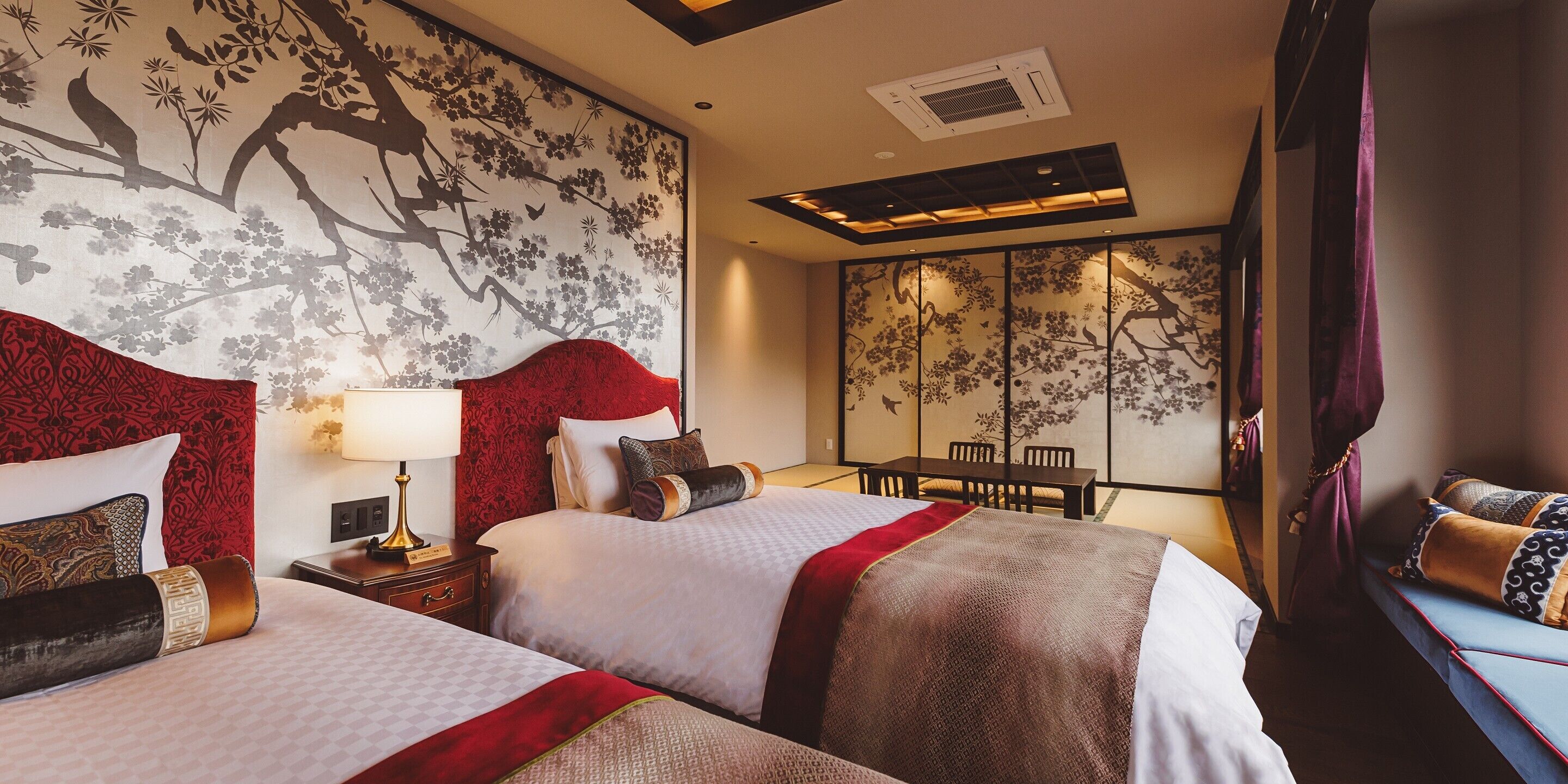 A hotel room with two beds, a dining table, and a traditional Asian-style wall mural.