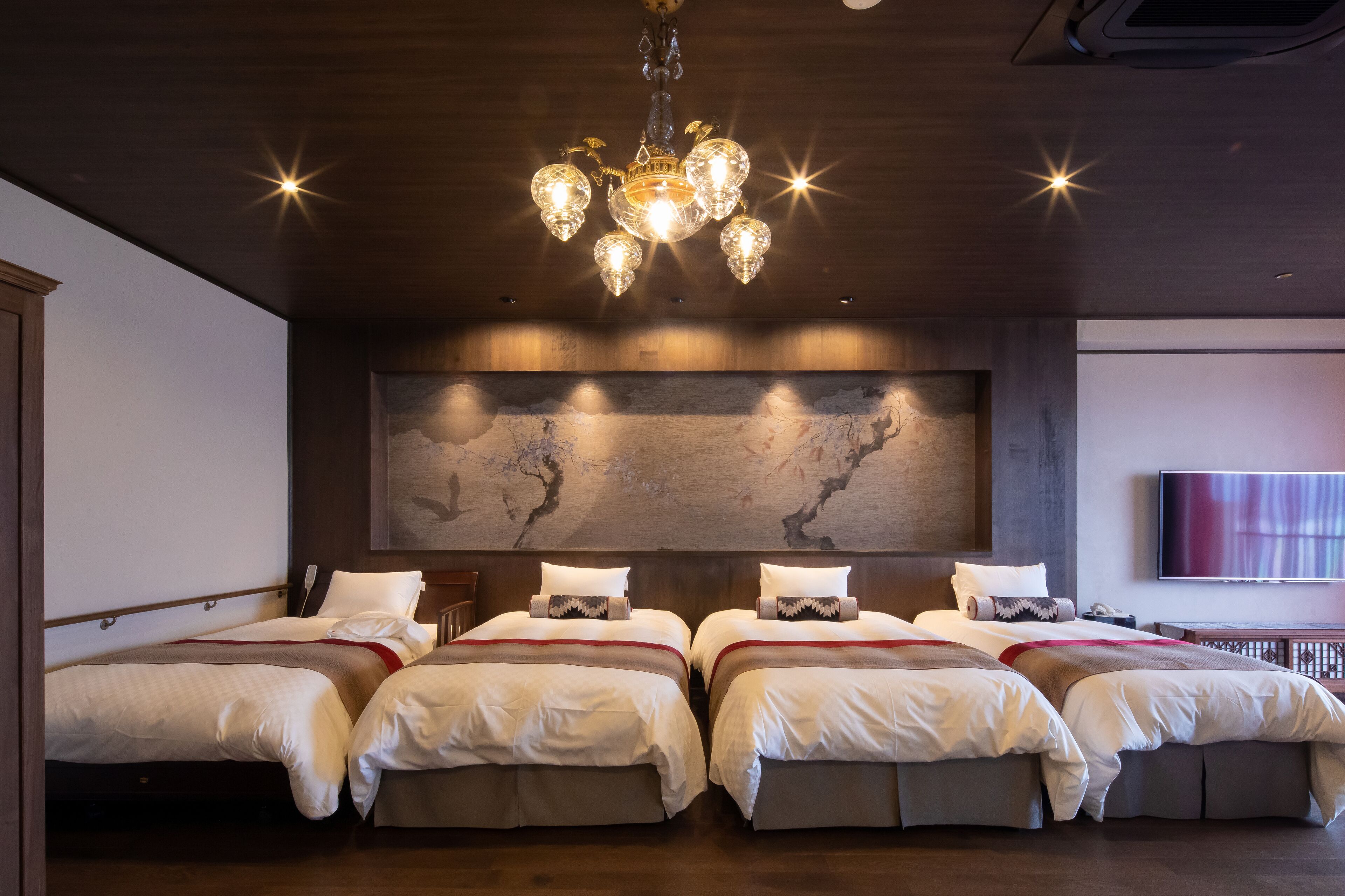 Une chambre d’hôtel avec quatre lits, une grande œuvre d’art accrochée au mur et un lustre moderne.