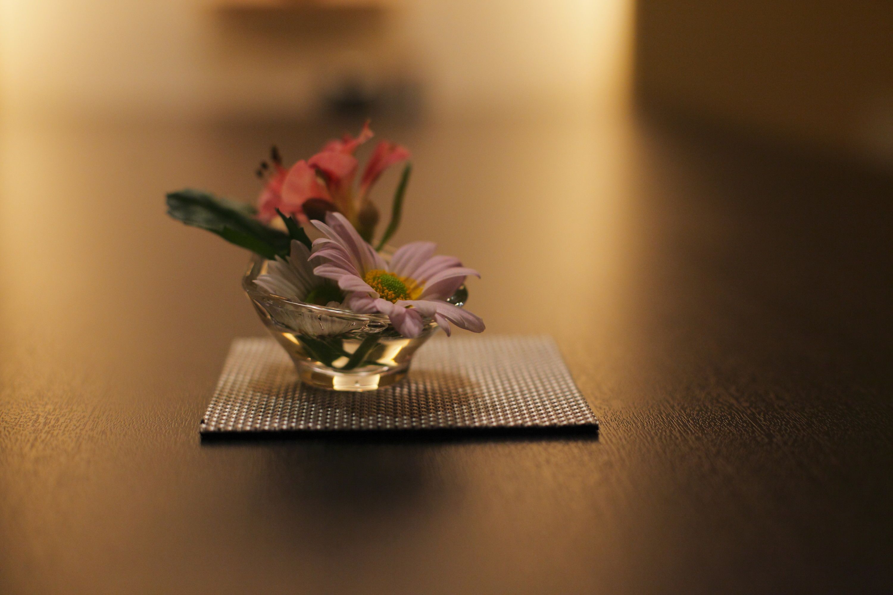 A small glass vase with flowers on a textured mat.