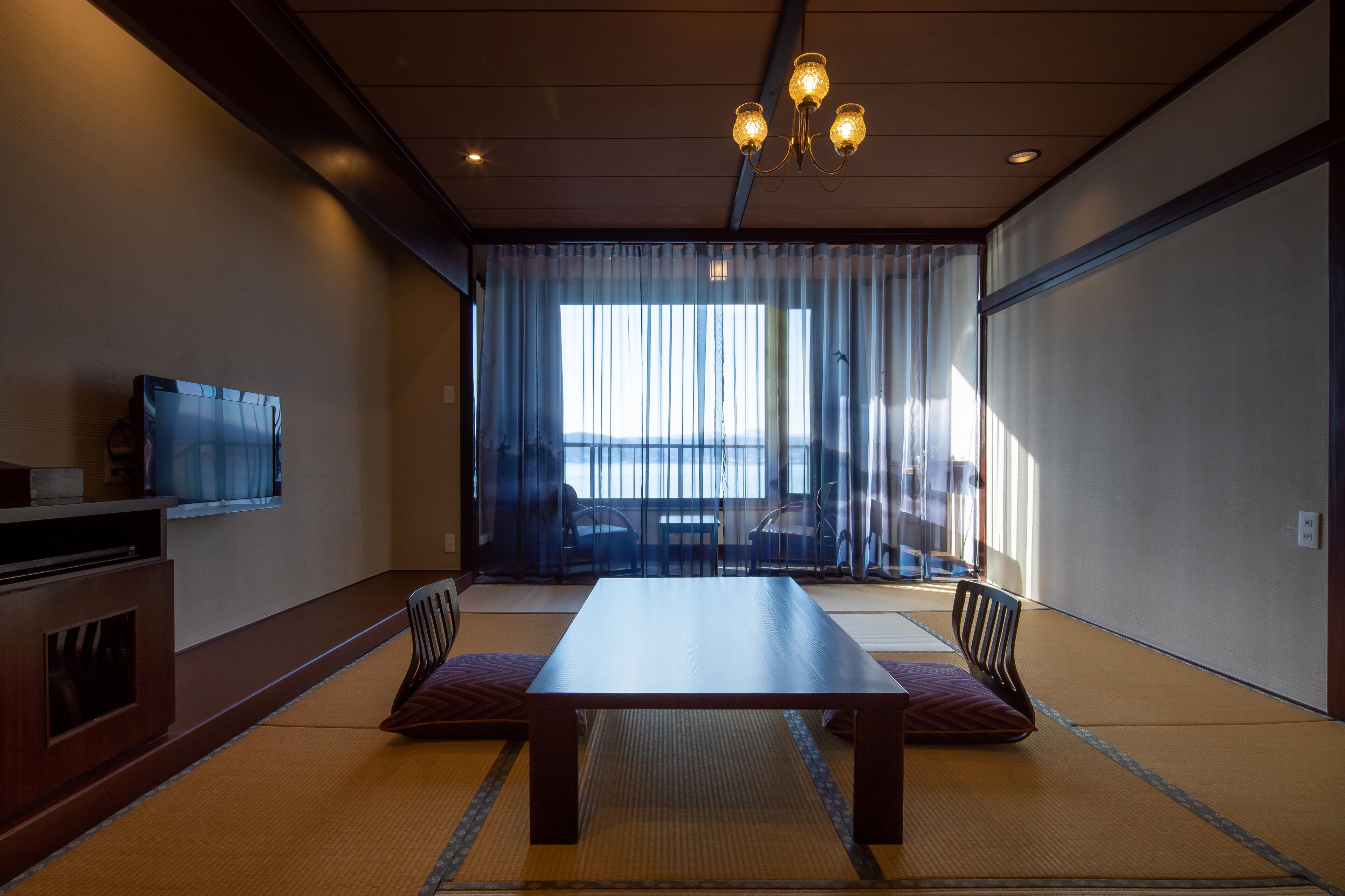 Una habitación tradicional japonesa con suelo de tatami, una mesa baja y un televisor sobre un mueble de madera.