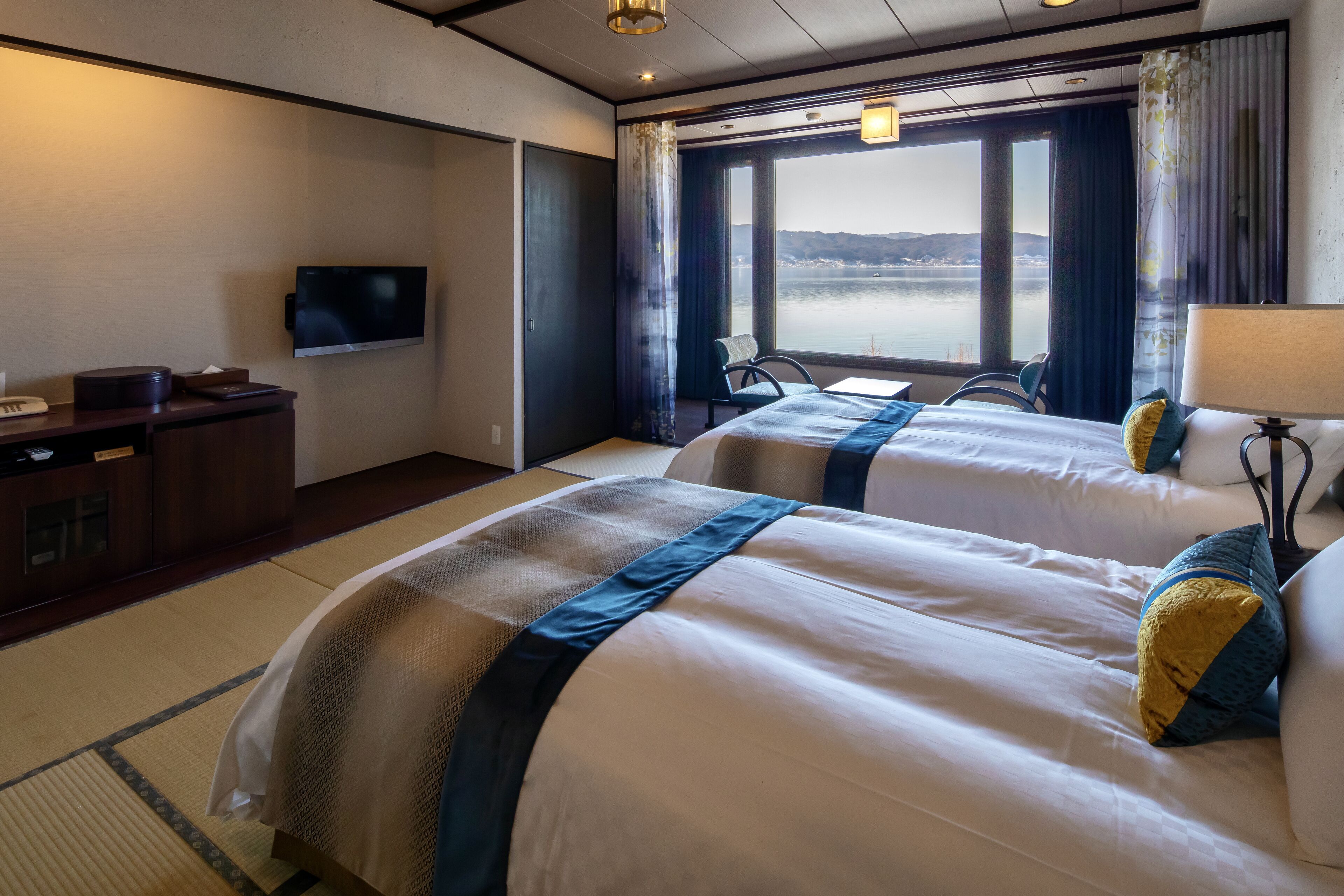 A hotel room with two beds, a TV, a desk, and a view of the water.