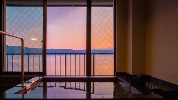 Una habitación con un ventanal grande que da a una masa de agua y montañas lejanas durante el atardecer.