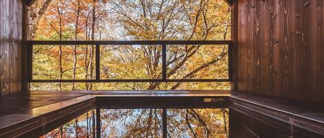 Eine Holzjagdhaus mit einem großen Fenster, das Bäume im Herbstlaub reflektiert.