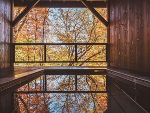 Une cabane en bois dotée d’une grande fenêtre qui reflète les arbres aux couleurs automnales.