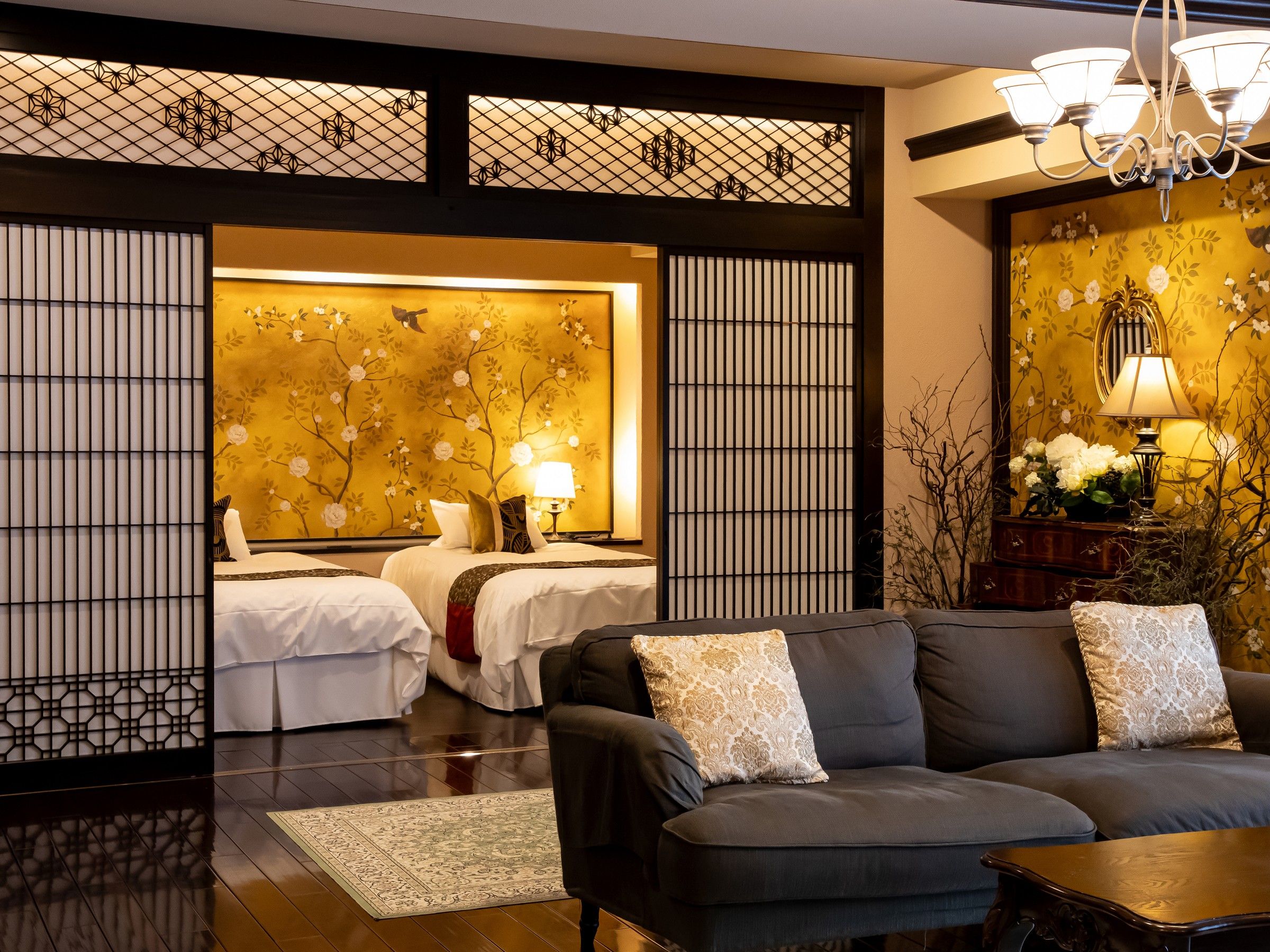 Habitación de hotel con diseño tradicional, que incluye un sofá, una cama con ropa de cama blanca y una pared decorativa con motivos florales.