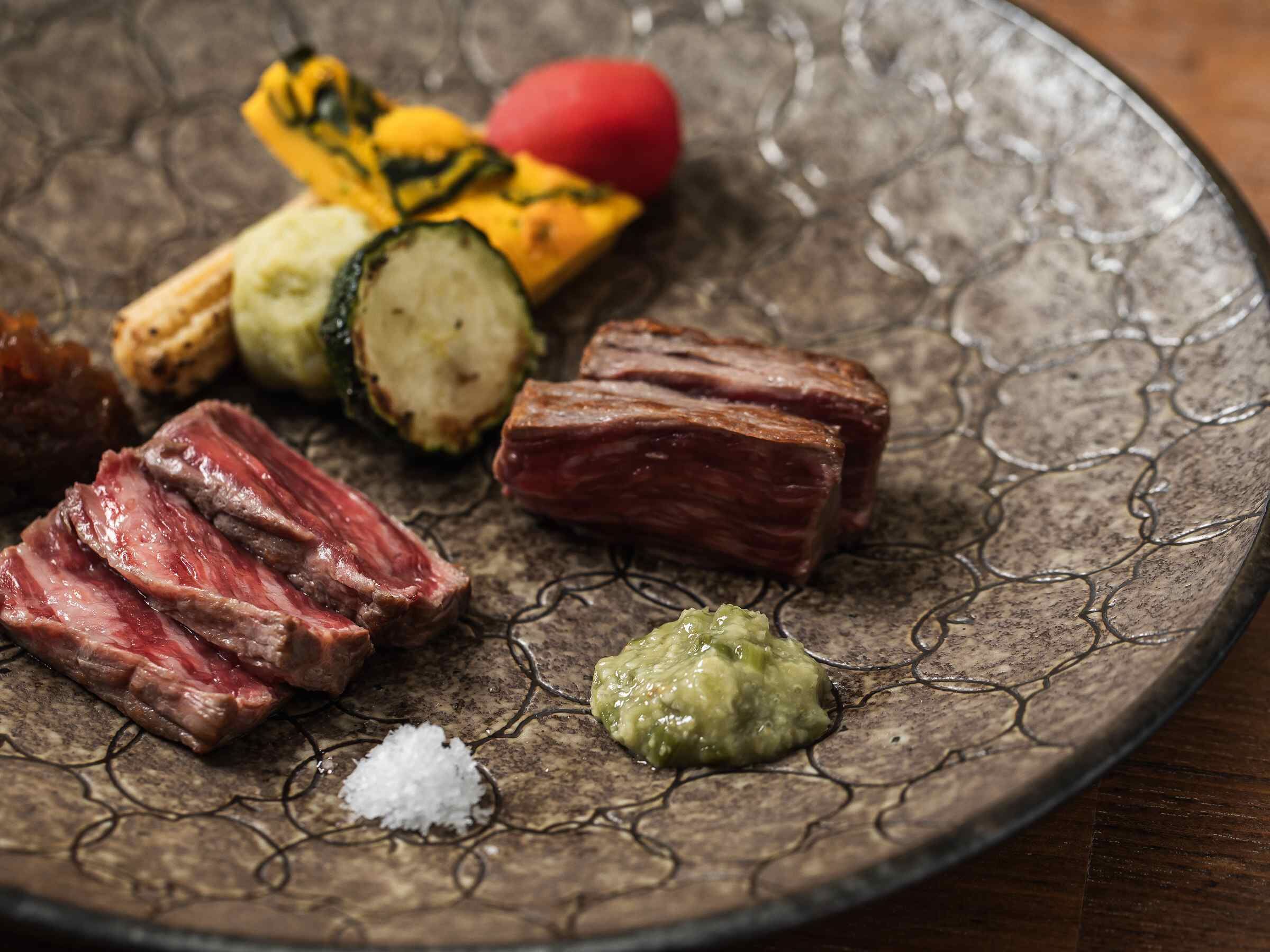 A plate with sliced meat, vegetables, and a green sauce.