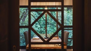 Une table en bois, une lampe, deux chaises et une fenêtre ornée d’un cadre géométrique.