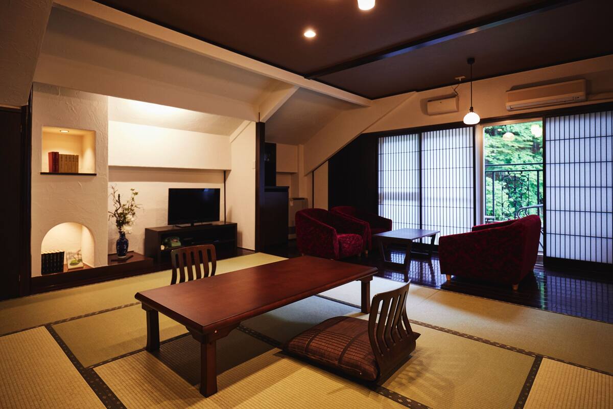 Ein traditioneller japanischer Wohnraum mit Tatami-Bodenbelag, einem niedrigen Tisch und roten Stühlen.