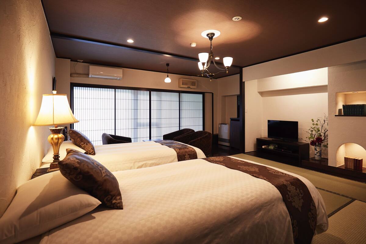 Ein Hotelzimmer mit zwei Betten, einem Fernseher, einem Schreibtisch und einem großen Fenster mit Jalousien.