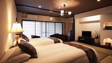 A hotel room with two beds, a television, a desk, and a large window with blinds.