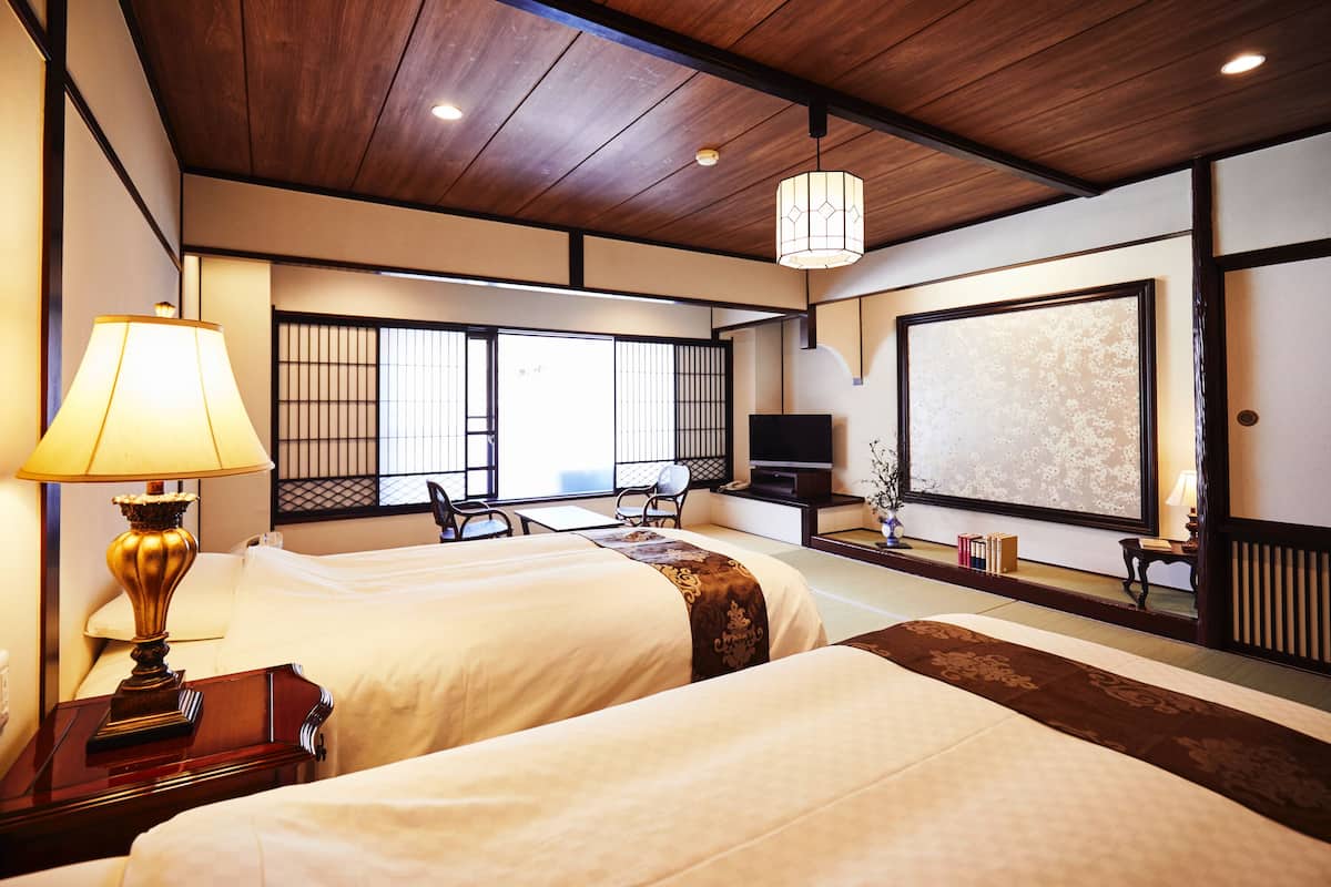 Ein traditionell japanisch gestaltetes Hotelzimmer mit zwei Betten, einem Fernseher und Blick durch Shoji-Schirme nach draußen.