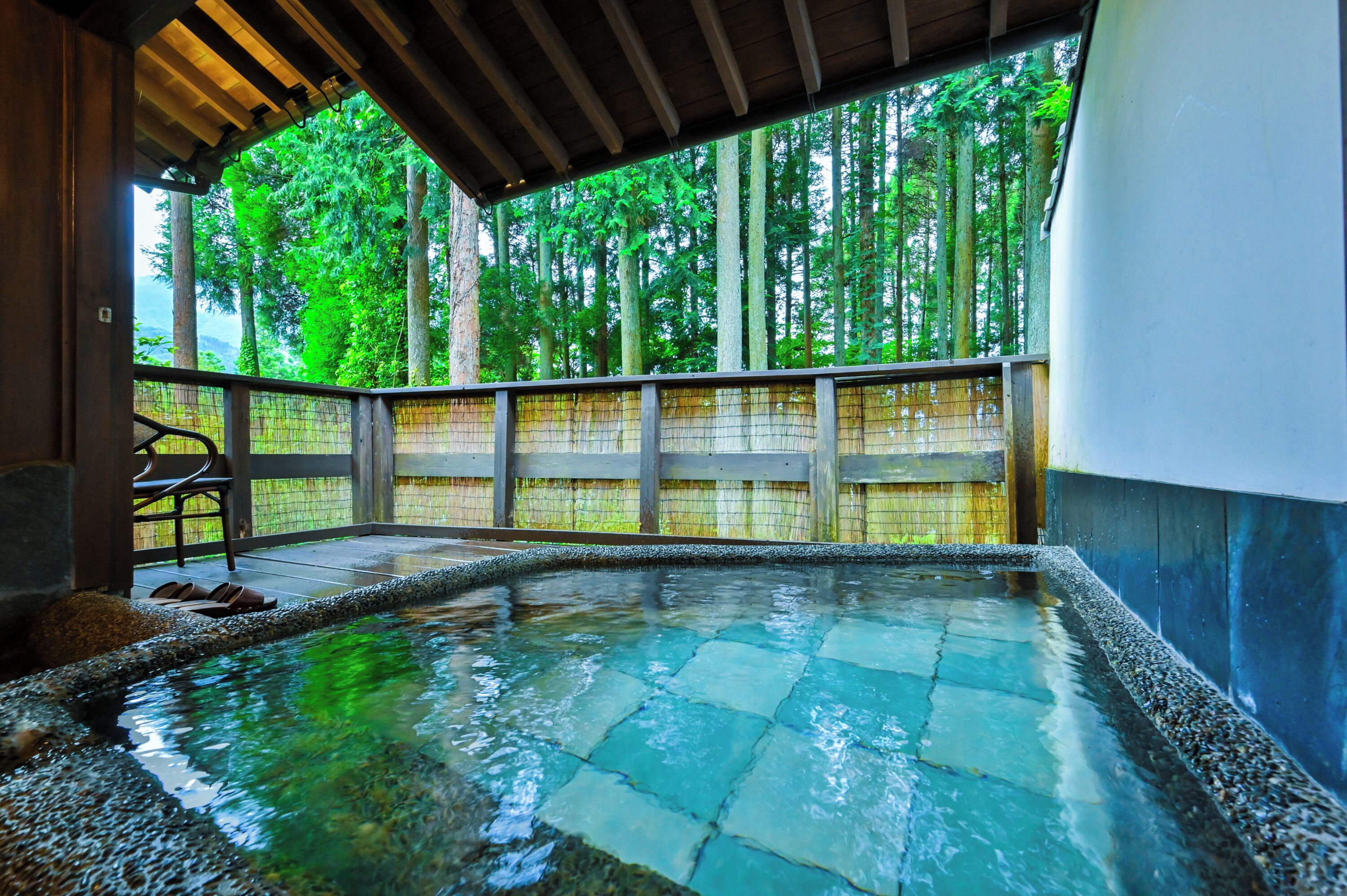A hot spring area with a wooden deck, stone tiles, and a view of a forest.