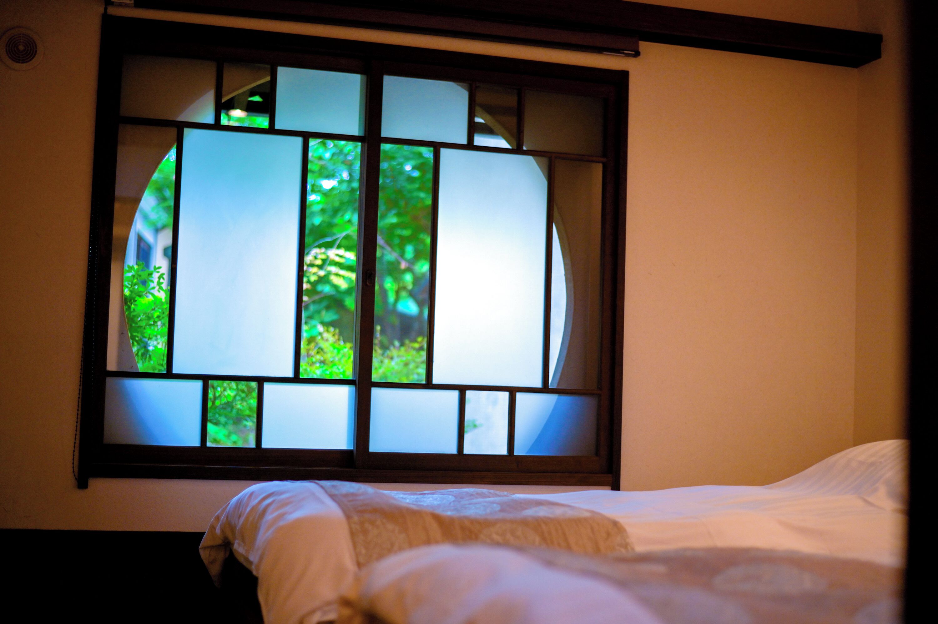 A room with a bed, a window with a view of greenery, and a wall-mounted air conditioning unit.