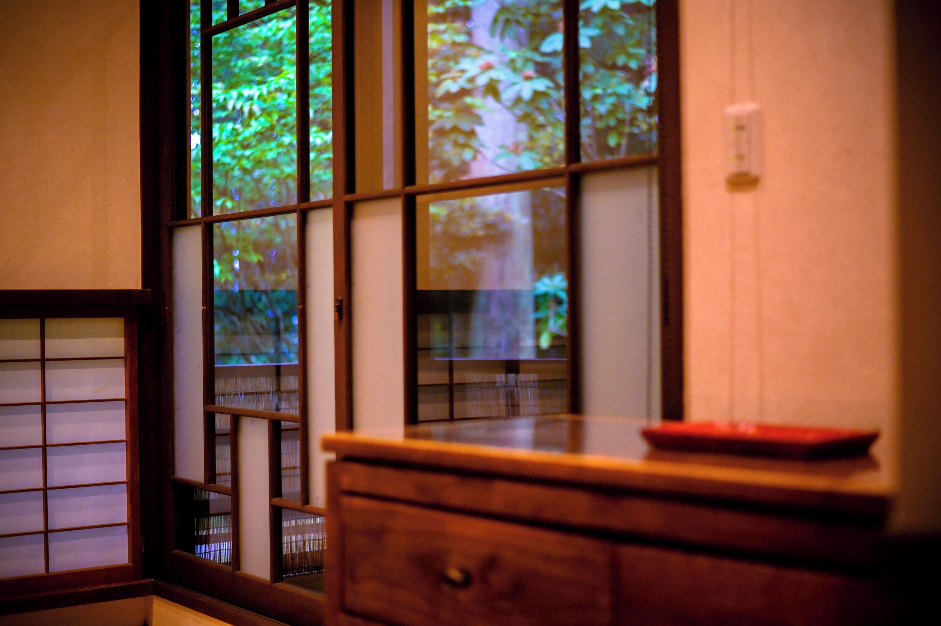 Una habitación japonesa tradicional con suelo de tatami, un escritorio de madera bajo y un puertas correderas con vista a la vegetación.