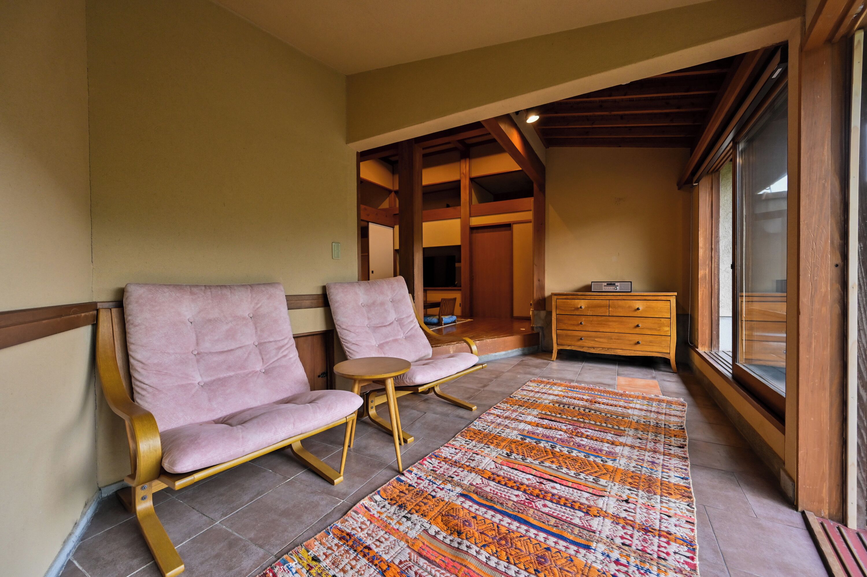 Ein Zimmer mit zwei gepolsterten Sesseln, einem kleinen runden Tisch, einer Holzkommode und einem gemusterten Teppich.