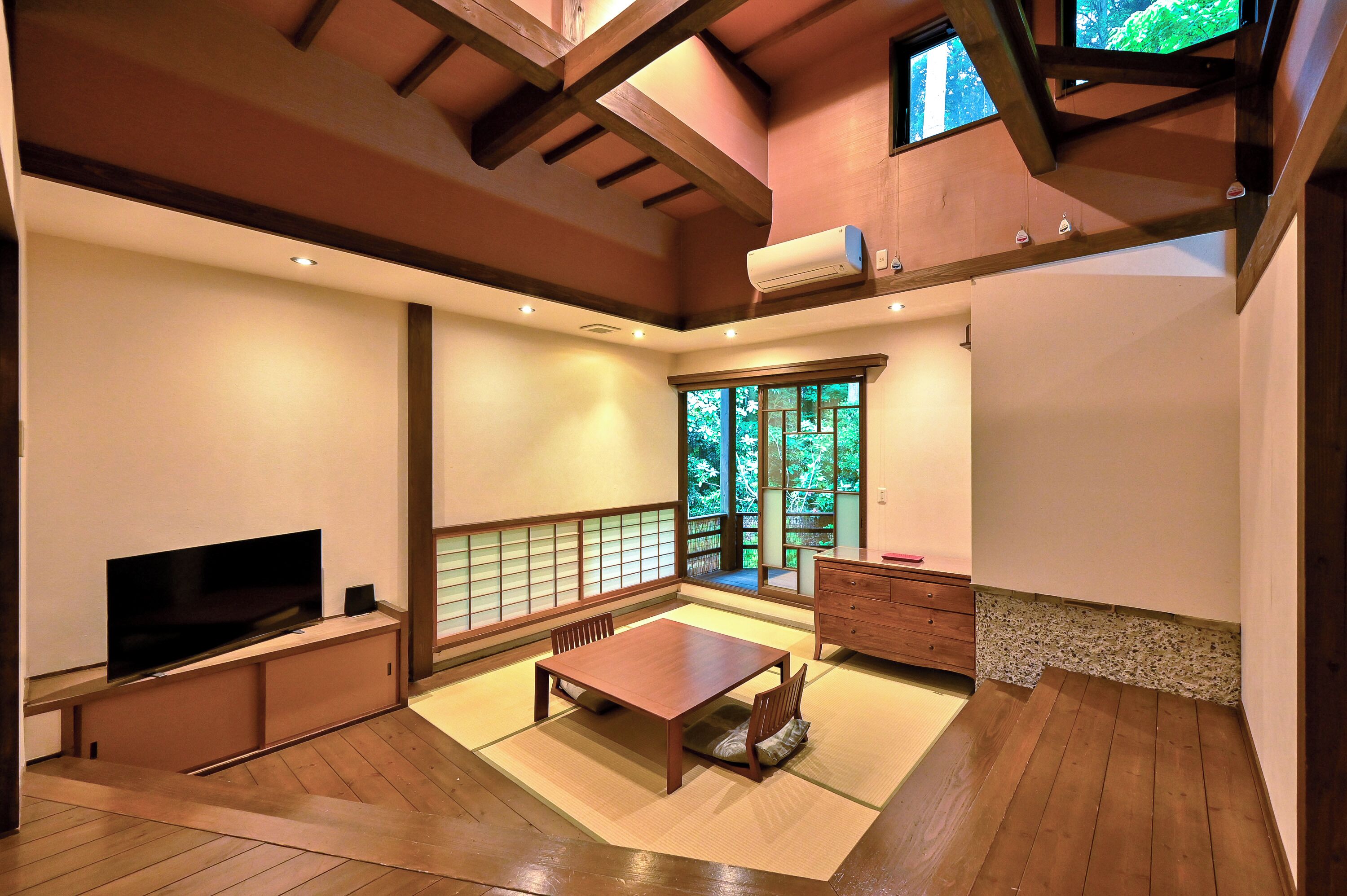A traditional Japanese-style room with tatami flooring, a low wooden table, a television, and a sliding door leading to a garden.
