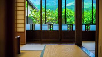 A traditional Japanese room with tatami flooring, shoji screens, and a view of greenery outside.