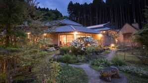A traditional Japanese house with a stone exterior, surrounded by a well-maintained garden with a pathway leading to the entrance.