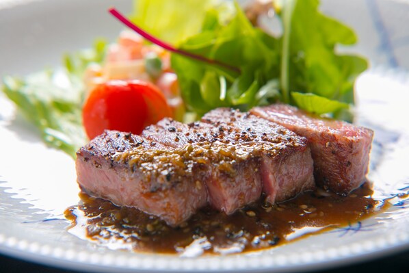 Un plato con un bistec a la parrilla, un tomate cherry y una ensalada de hojas verdes.