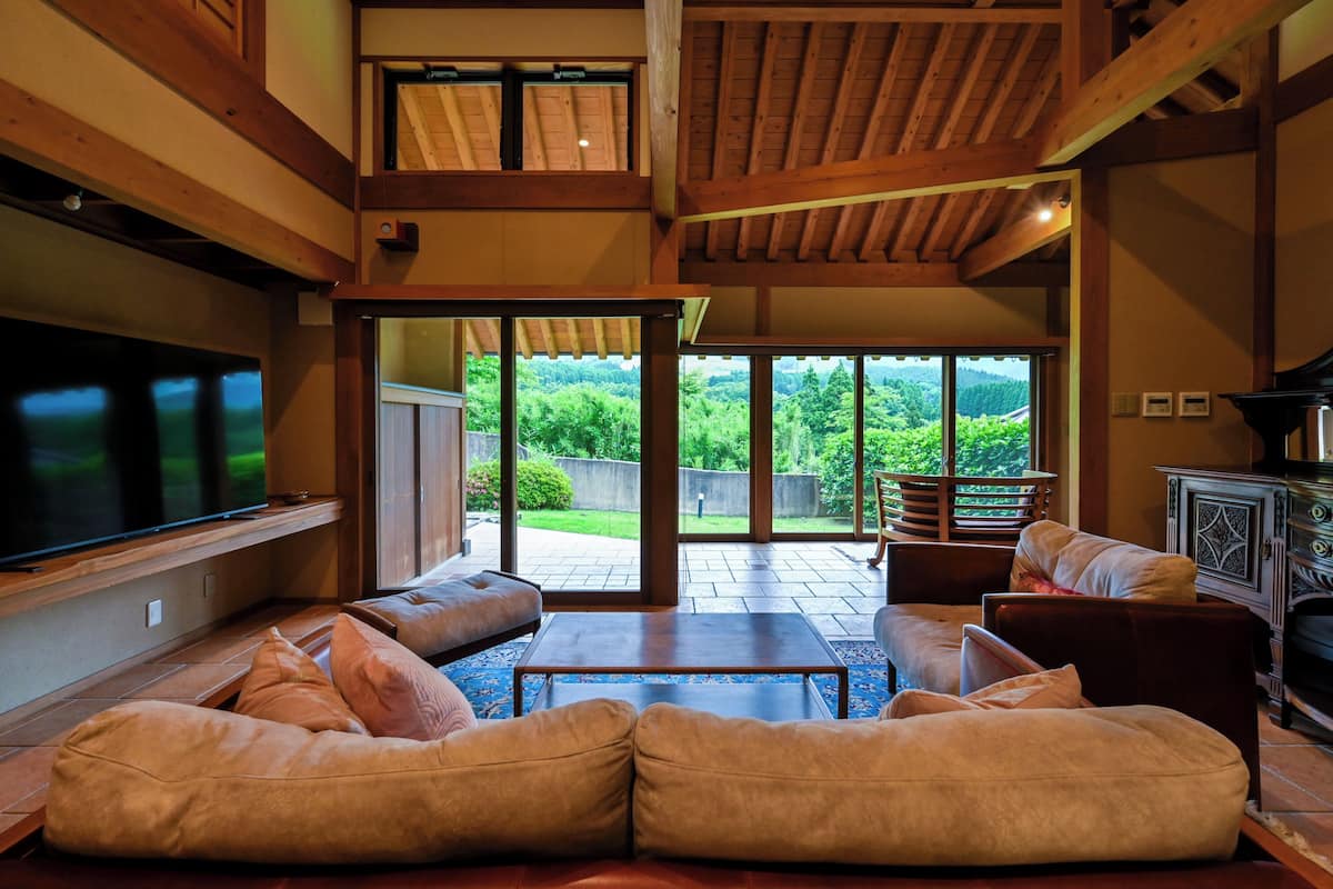 Un salon spacieux doté d’un grand téléviseur, de sièges confortables et offrant une vue sur un jardin luxuriant grâce à de grandes portes vitrées.