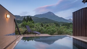 An infinity pool with a view of mountains, a lounge chair, and a wooden deck.