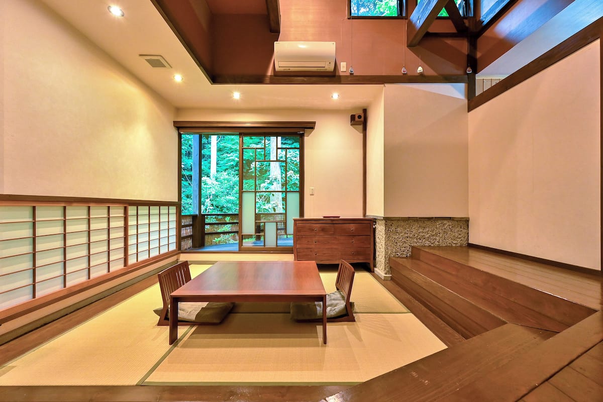 Une pièce de style japonais traditionnel, avec un sol recouvert de tatamis, une petite table en bois et une porte coulissante donnant sur un jardin.