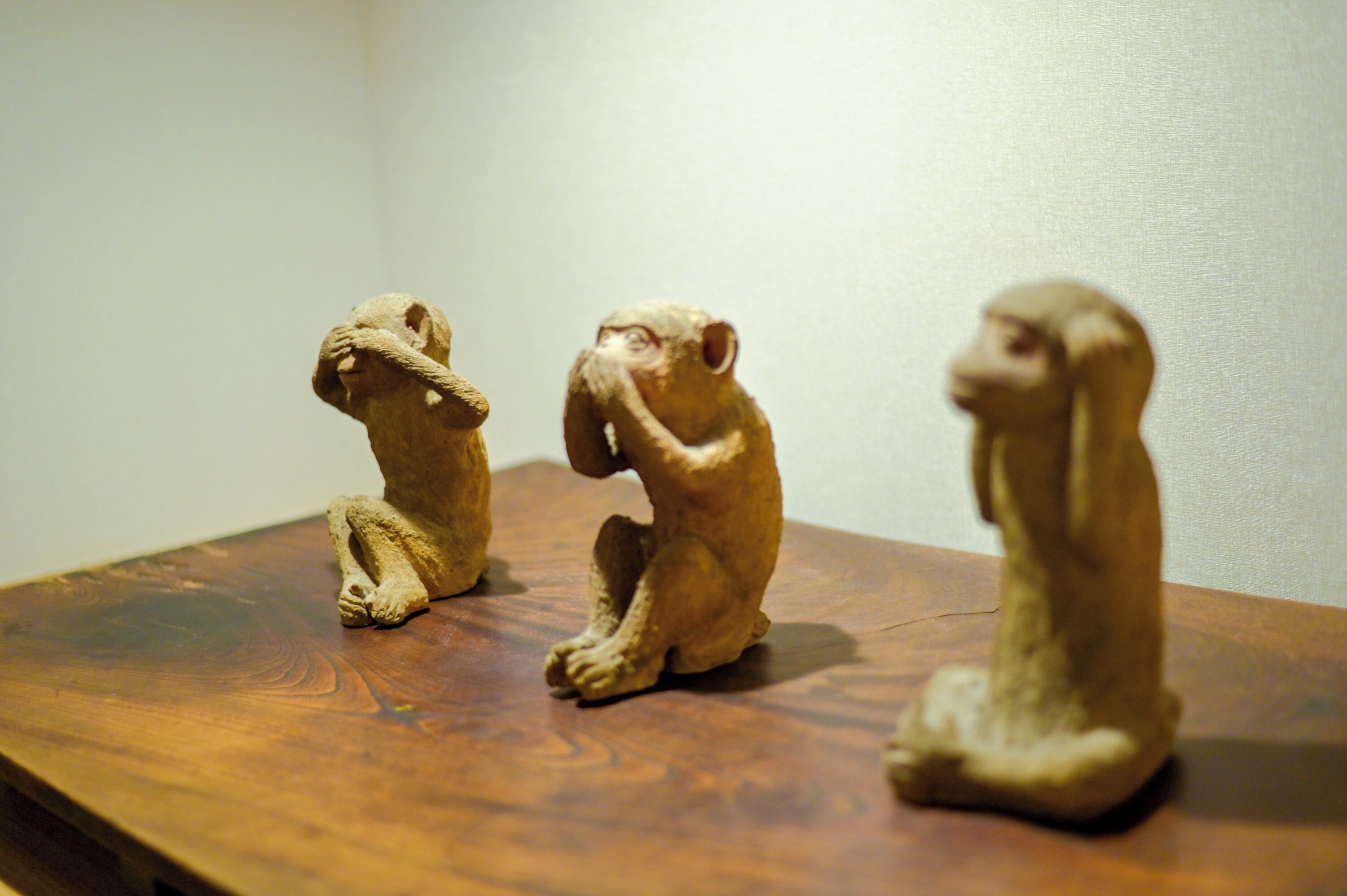 Three small, beige, seated figurines on a wooden surface.
