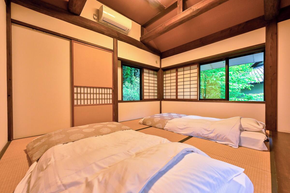 Une pièce de style japonais traditionnel, avec un sol recouvert de tatamis, des portes coulissantes et une vue sur la verdure par les fenêtres.