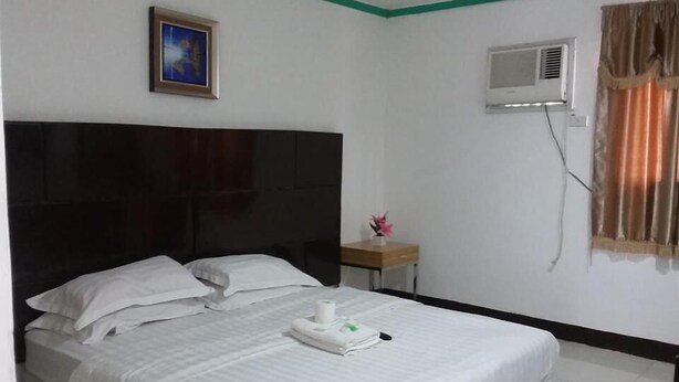 A hotel room with a large bed, a bedside table with a vase of flowers, an air conditioning unit, and a framed picture on the wall. - Asia Novo Boutique Hotel - Roxas (Roxas City)