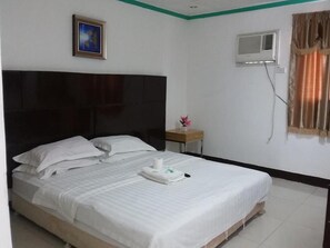 Een hotelkamer met een groot bed, een nachtkastje met een bloevas, een airconditioningapparaat en een lijst aan de muur.