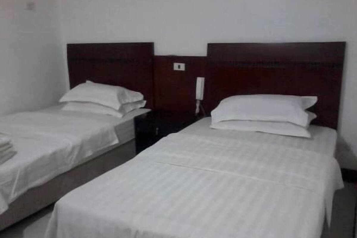 Habitación de hotel con dos camas individuales, cada una con ropa de cama blanca y cabeceros de madera.