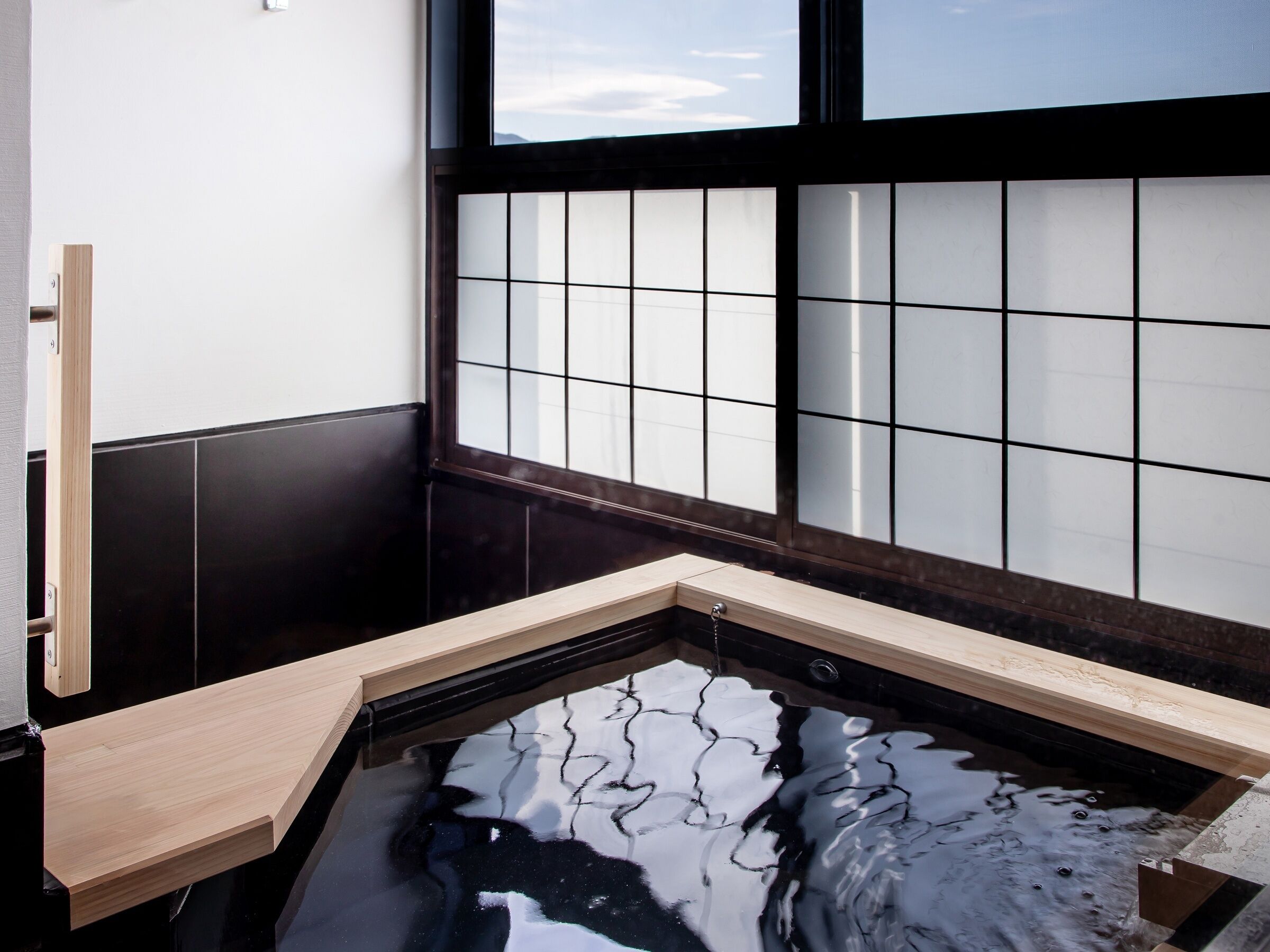 A traditional Japanese-style room with a tatami mat floor, a shoji screen, and a small onsen (hot spring) tub.