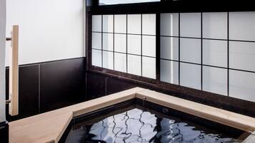 A traditional Japanese-style room with a tatami mat floor, a shoji screen, and a small onsen (hot spring) tub.