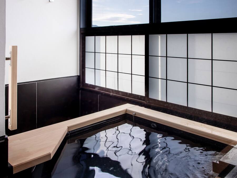 A traditional Japanese-style room with a tatami mat floor, a shoji screen, and a small onsen (hot spring) tub.