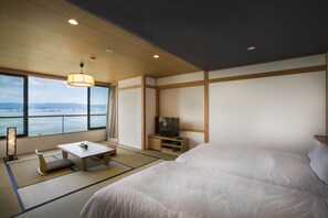 A hotel room with a large bed, a TV, a small table, and a view of the water. - Sui Suwako (Suwa)