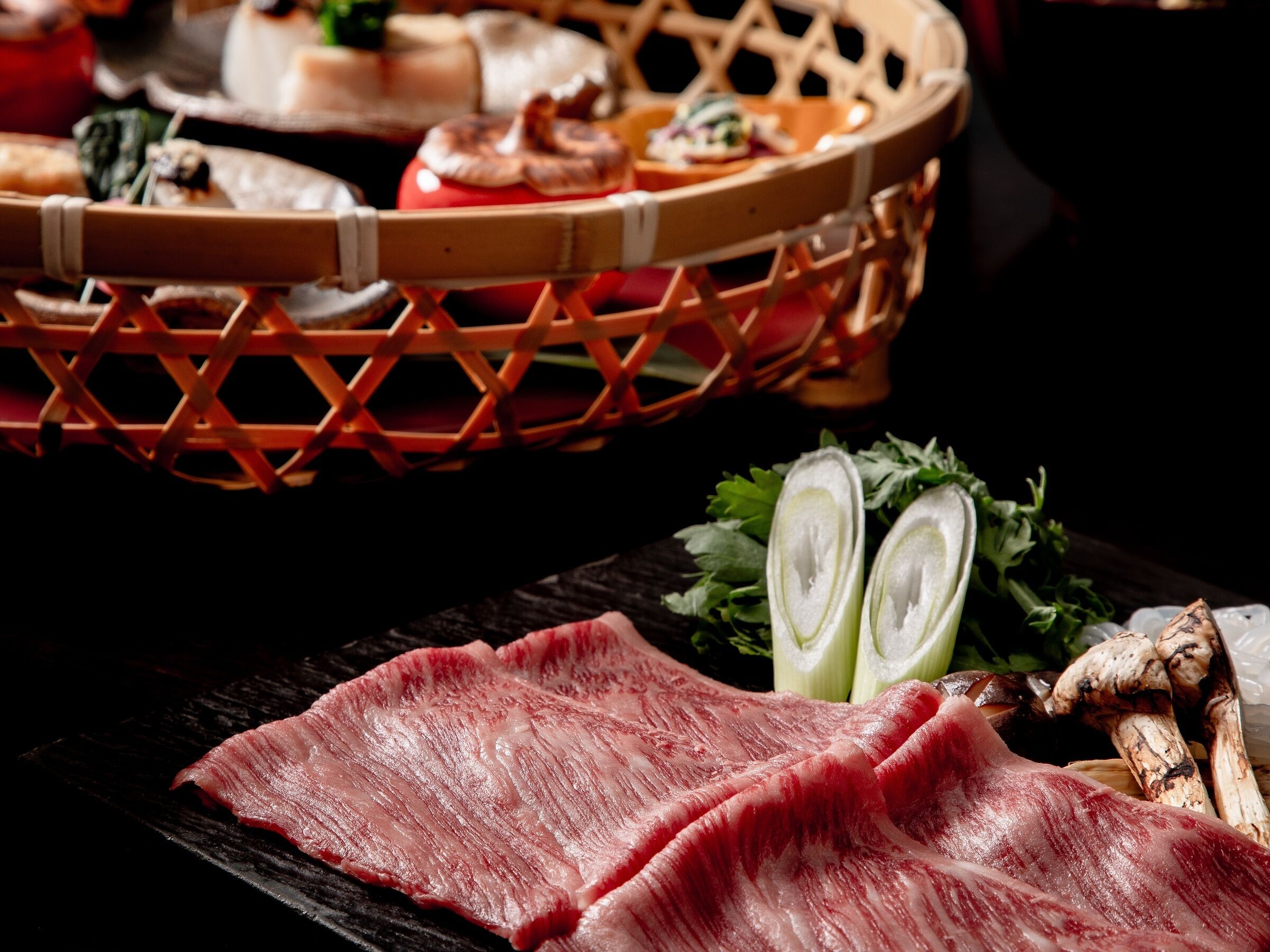 A wooden table with raw meat, sliced vegetables, and mushrooms.