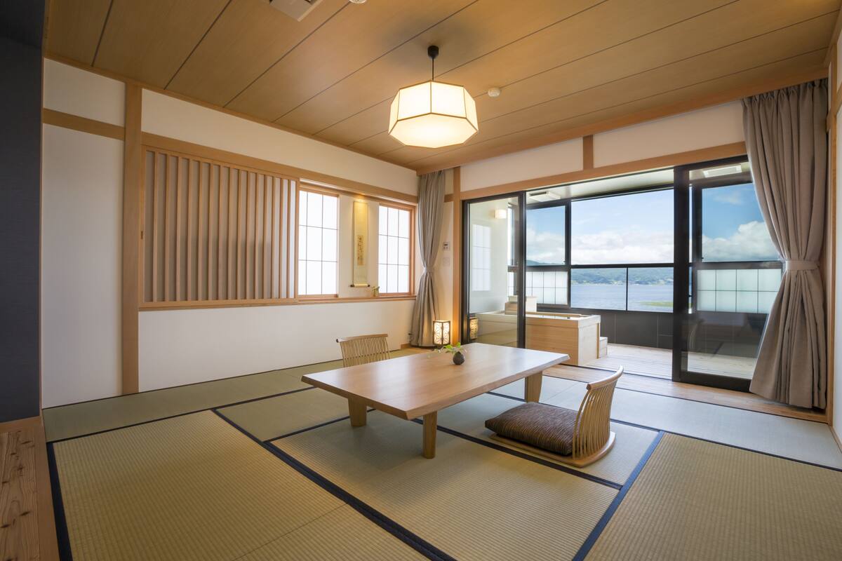 A traditional Japanese room with tatami flooring, a low wooden table, and a view of the sea through large windows.
