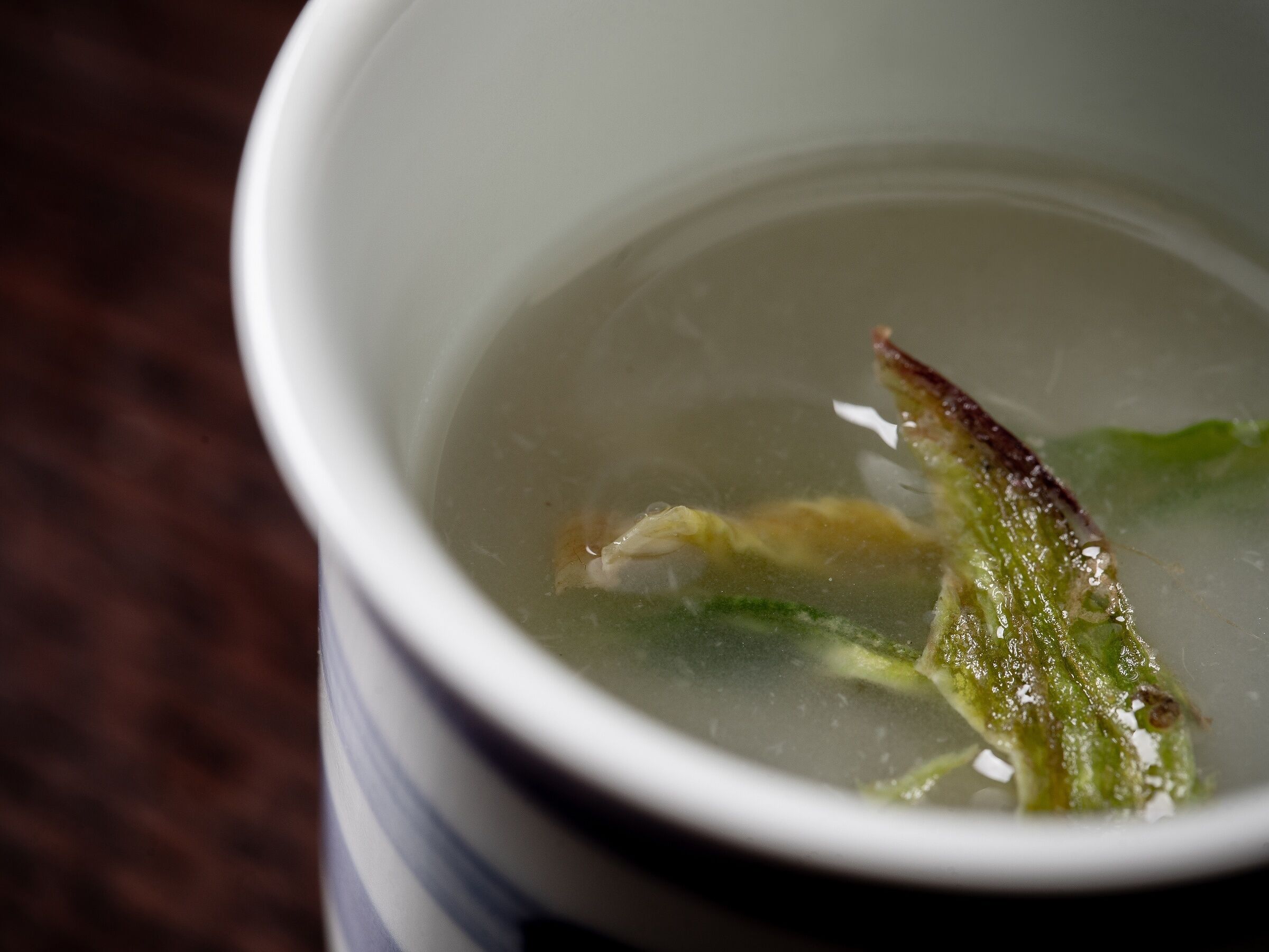 Une vue rapprochée d’un liquide transparent dans une tasse, dans lequel flotte un objet vert.