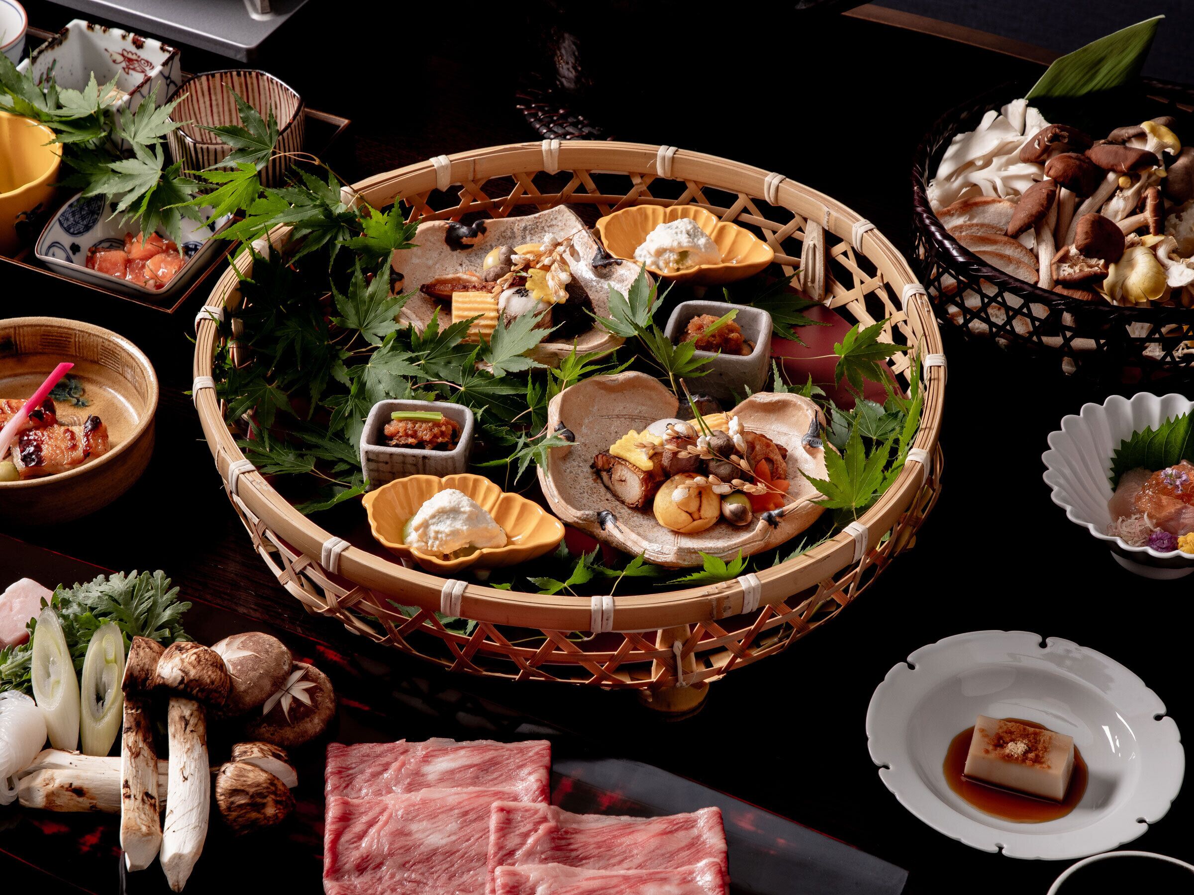 Presentación tradicional japonesa de comida con diversos platos e ingredientes expuestos en una cesta tejida.