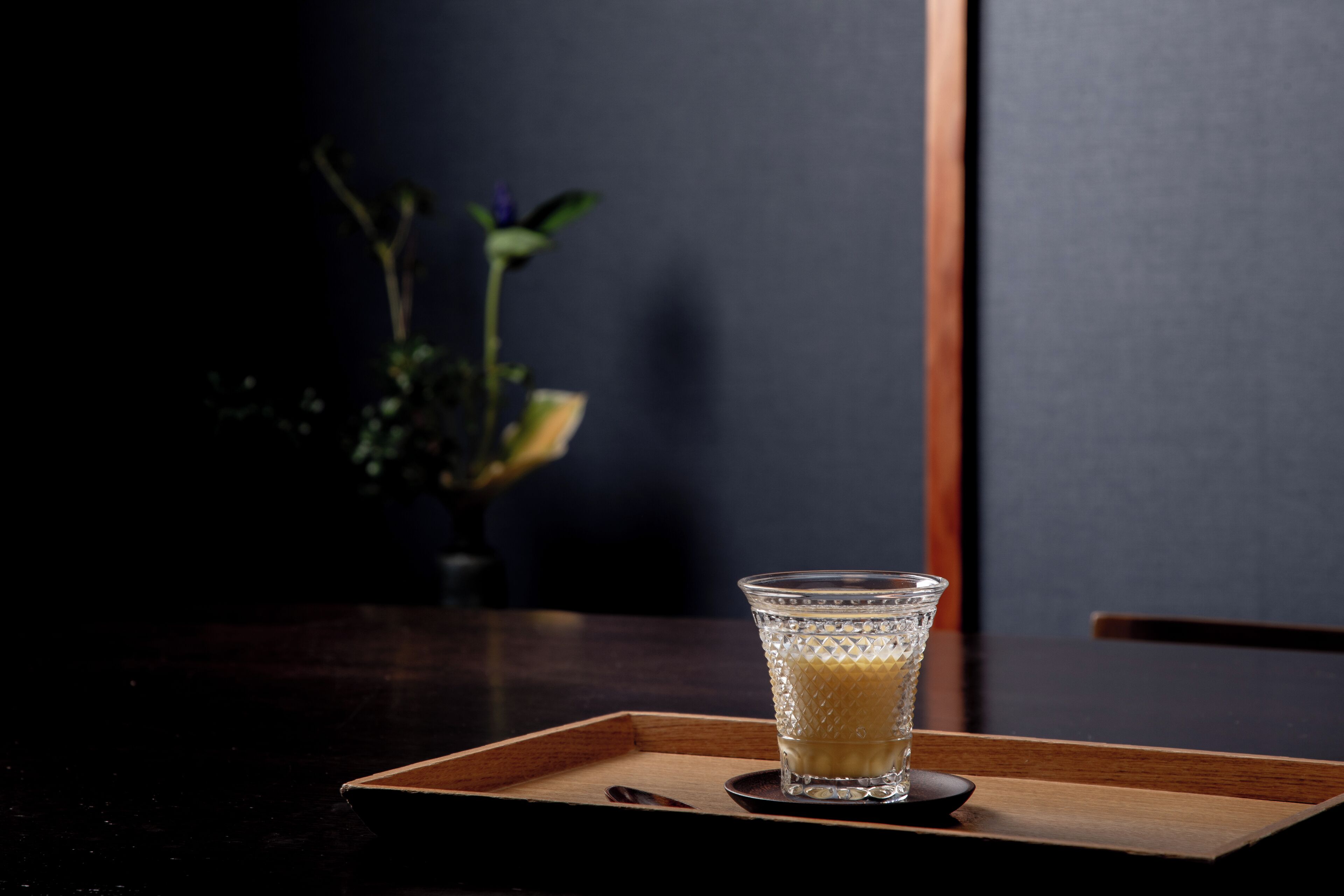 A glass of a clear liquid on a wooden tray.