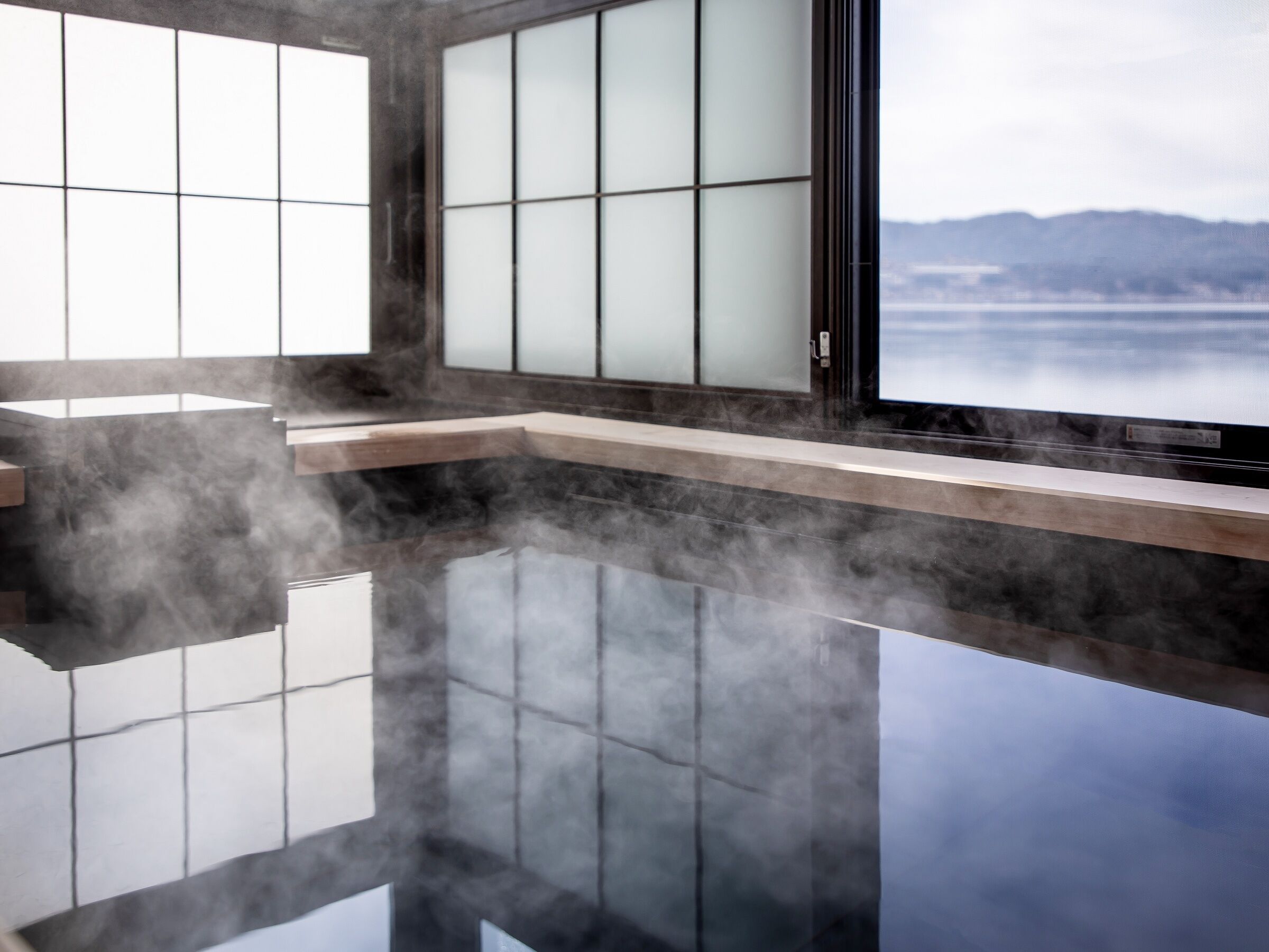 A modern bathroom with a large mirror, steam feature, and a view of a body of water and mountains.