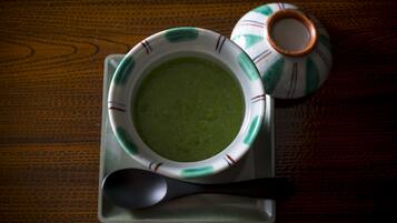 A bowl of green soup on a tray with a spoon and a decorative pot.