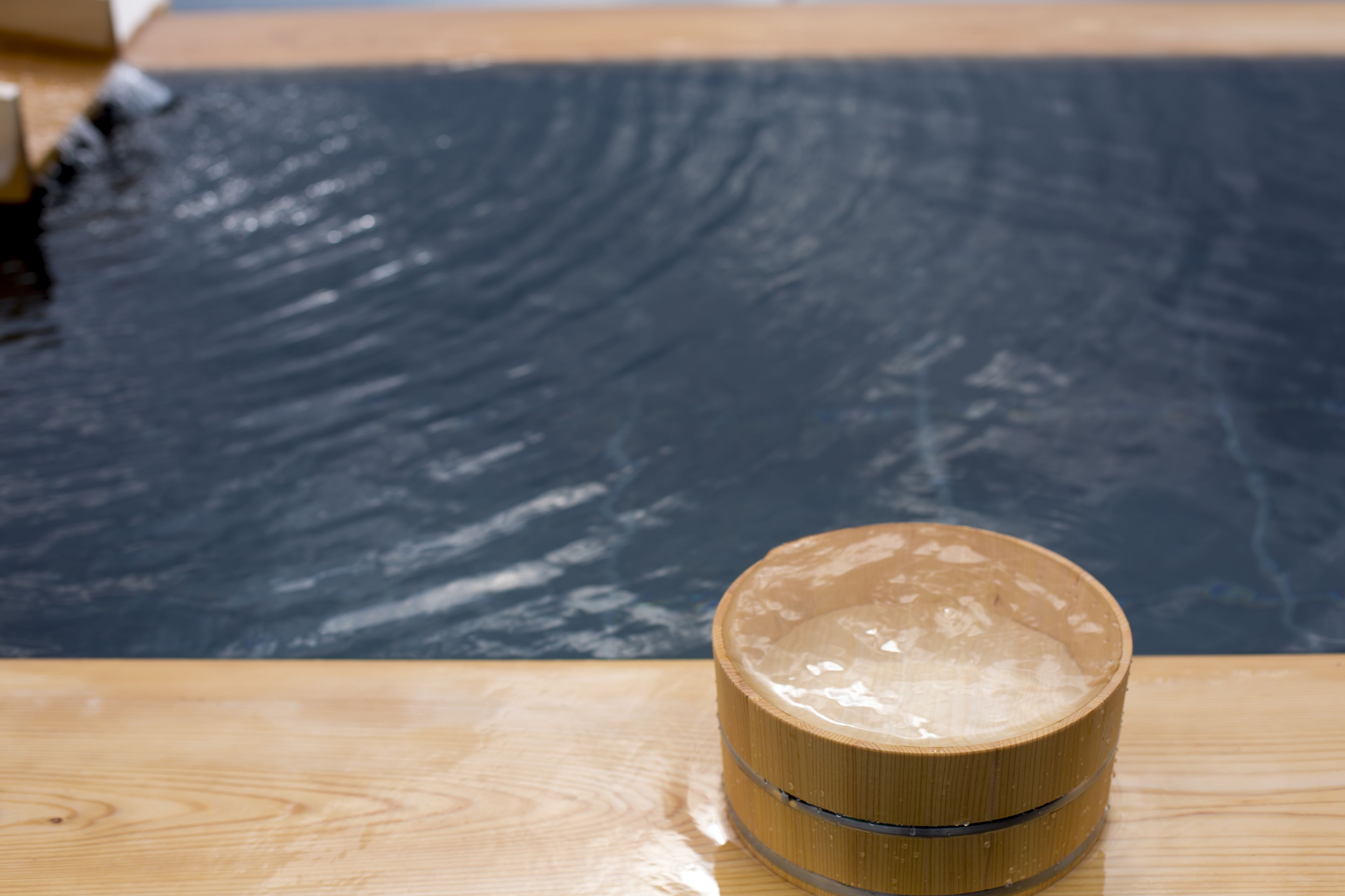 A wooden table with a round container on it, placed in front of a pool.