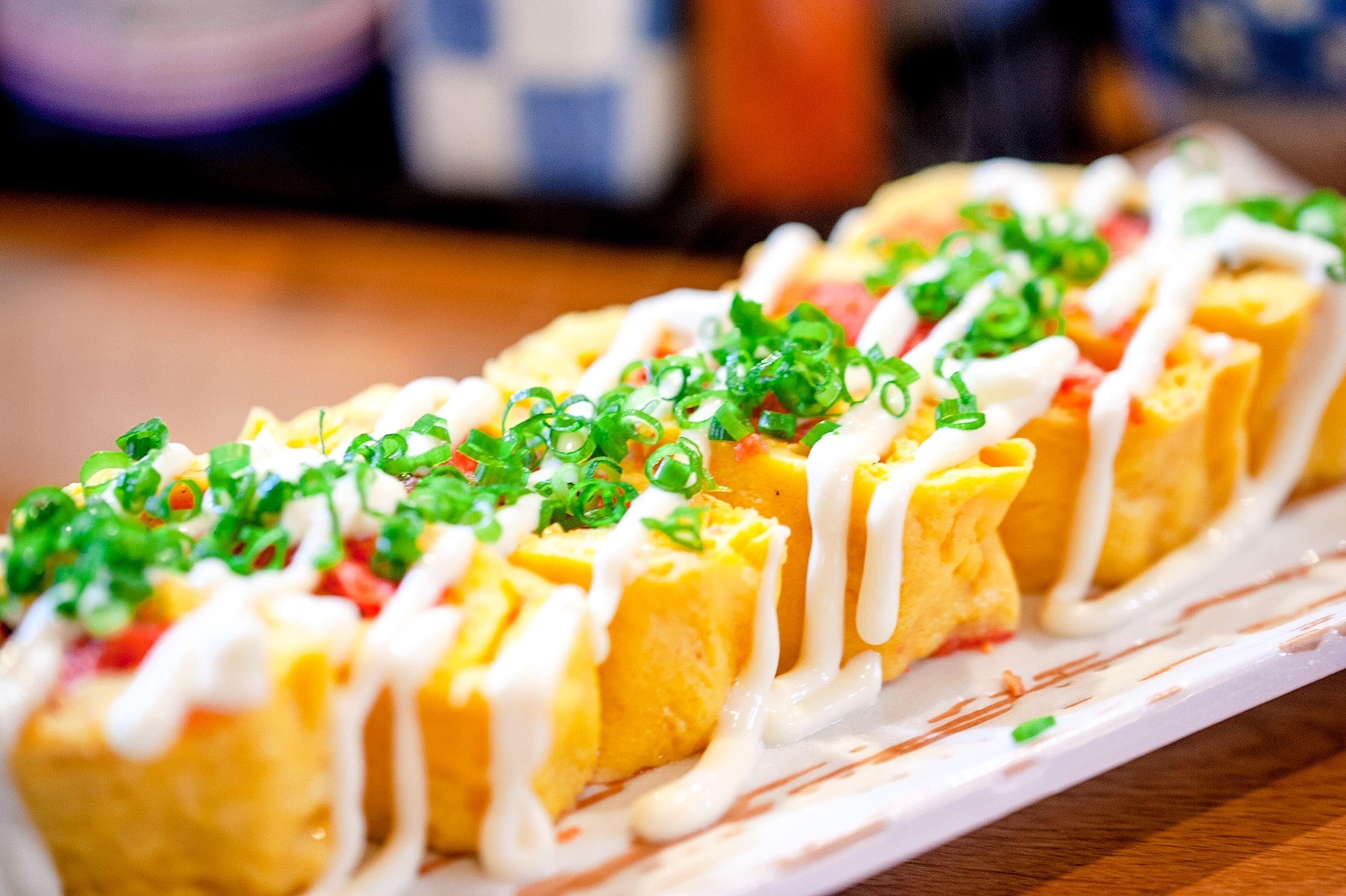 A dish with sliced omelettes topped with green onions and white sauce.