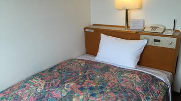 Una habitación de hotel con cama, lámpara de noche, teléfono y panel de control en la cabecera.