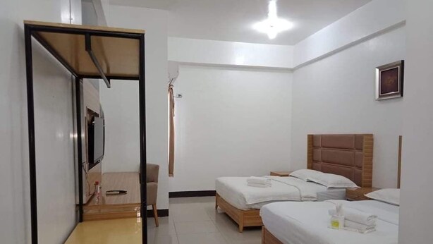 Hotellihuone, jossa on kaksi sänkyä, puinen pääty, peili ja pieni pöytä.