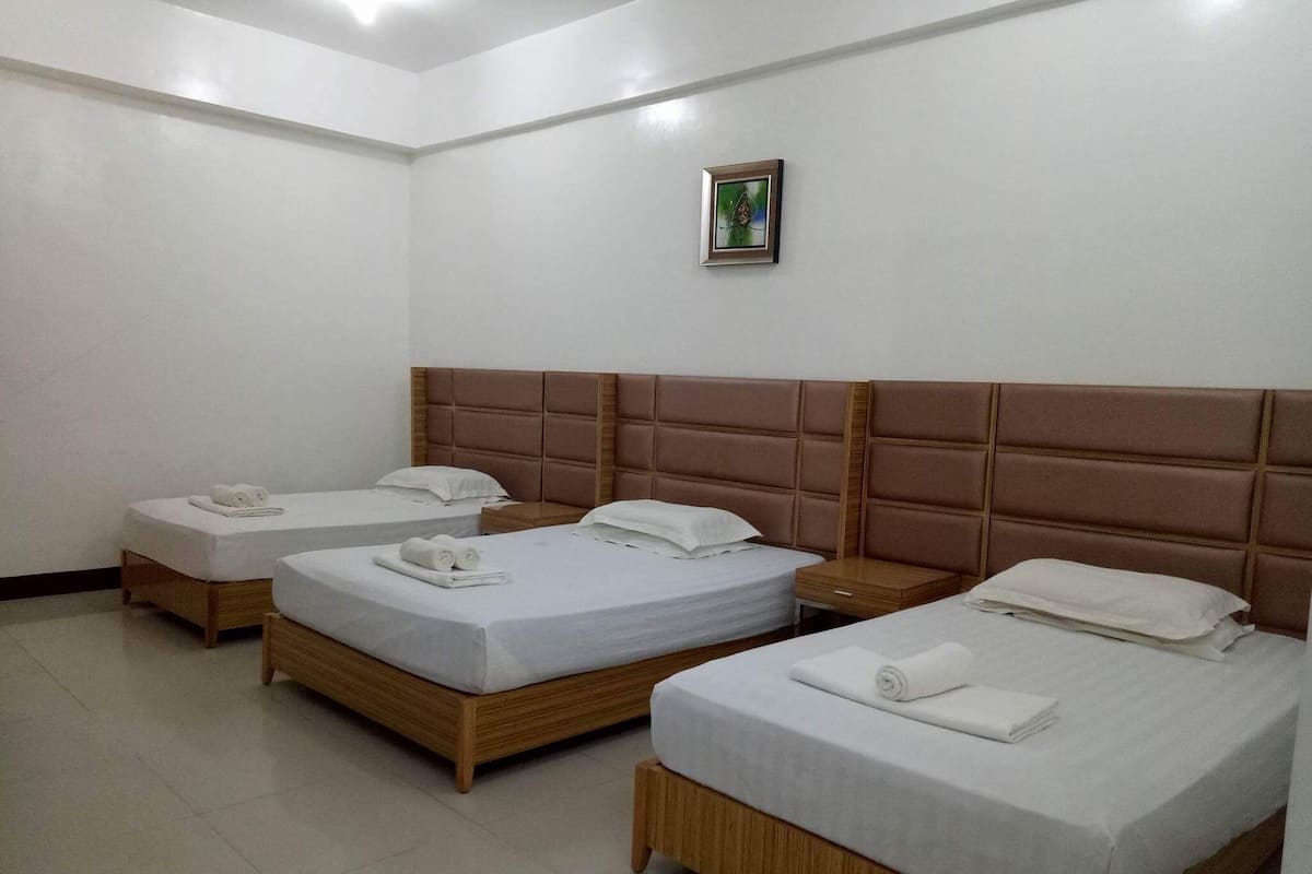 Ein Hotelzimmer mit drei Einzelbetten, jeweils mit Holzrahmen und Kopfteil.