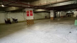 Maanalainen pysäköintihalli, jossa on betonilattiat ja -seinät, kaksi moottoripyörää on pysäköitynä, ja pylväissä on varoituskylttejä.